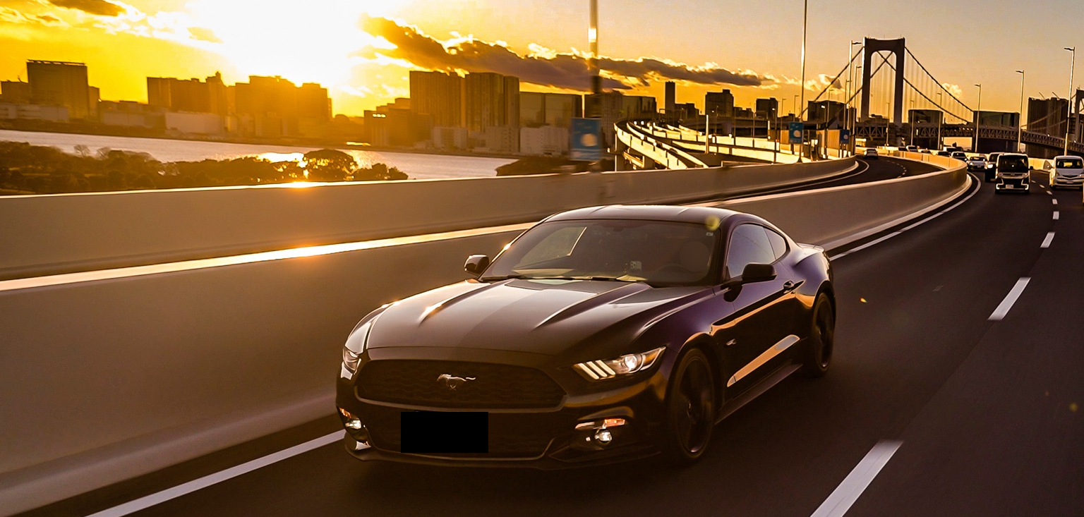 夕焼けの高速道路を走る黒いフォード・マスタング